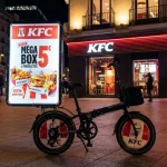 Bicivalla publicitaria nocturna de la marca KFC con promoción Mega Box frente a sucursal activa
